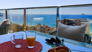 A balcony with a table set for breakfast, a glass of orange juice, and a croissant. - SUNSET CLIFFS sea view apartments (Benidorm)