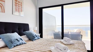 A modern hotel room with a large bed, two pillows, a view of the city, and a balcony with a chair. - SUNSET CLIFFS sea view apartments (Benidorm)