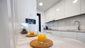 Eine moderne Küche mit weißen Schränken, einer Edelstahlspüle und zwei Gläsern Orangensaft auf einer rundlichen, gepunkteten Unterlage.
