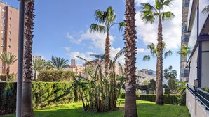 A courtyard with palm trees, a grassy area, and a building with balconies. - ESTRELLA design & beach apartment (Benidorm)