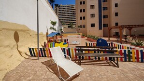 A sunny outdoor area with a white sun lounger, a wooden bench, and a colorful play structure. - ESTRELLA honey apartment (Benidorm)