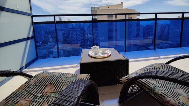 A balcony with a table set for tea, wicker furniture, and a city view. - ESTRELLA honey apartment (Benidorm)