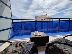 Un balcon avec une table préparée pour le thé, des meubles en osier et une vue sur la ville.