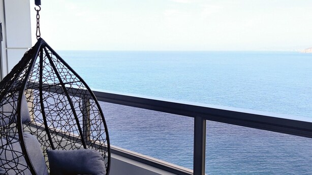 Un balcon avec un fauteuil suspendu et des sièges rembourrés, donnant sur une mer calme.