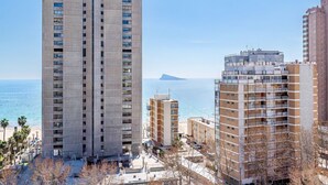 Un edifici de grattacels amb diverses plantes, una platja al fons i un cel serè.