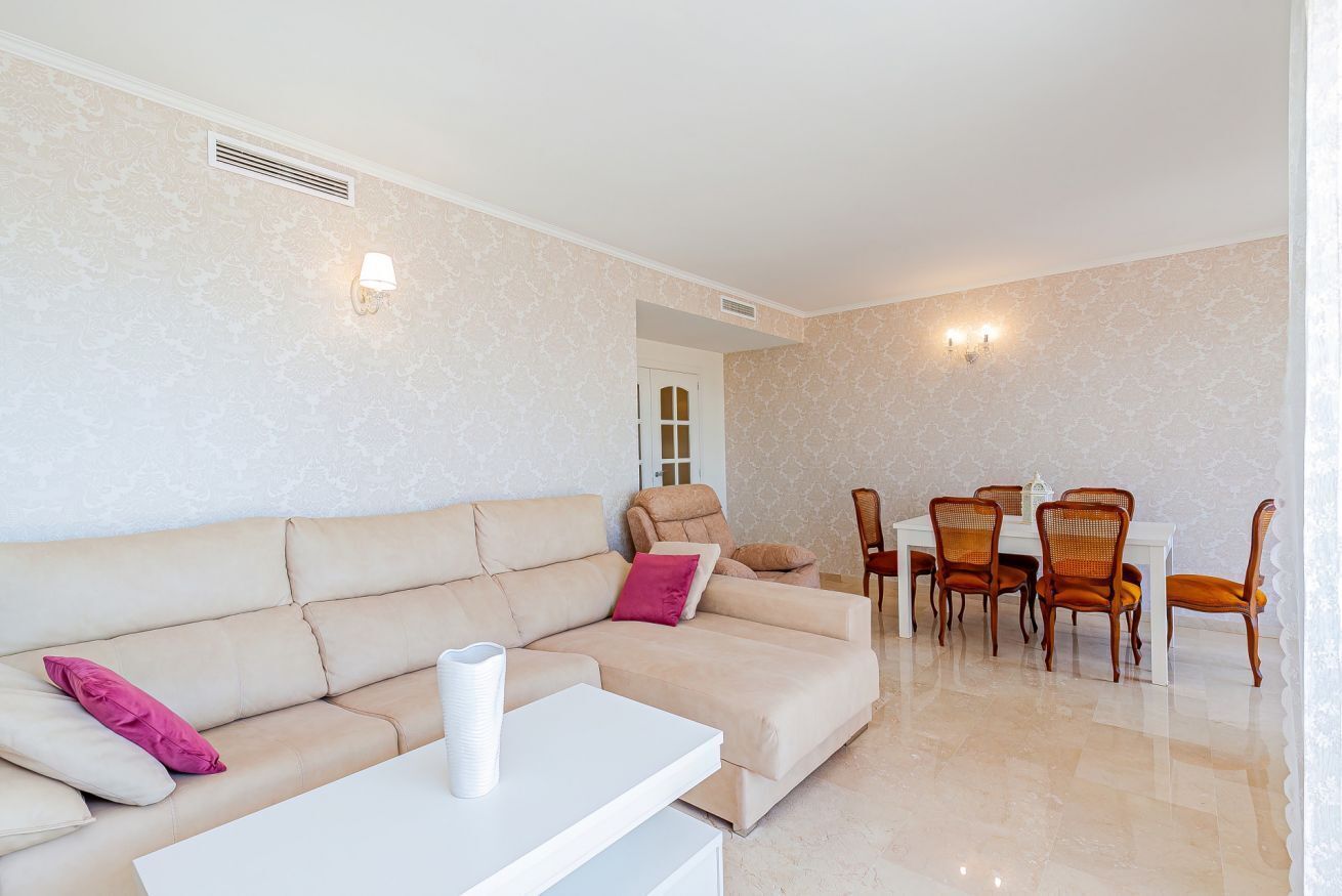 Una sala de estar con un sofá color beige, una mesa de centro blanca y un comedor con sillas de madera y una mesa blanca.