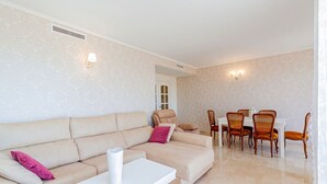 A living room with a beige sofa, a white coffee table, and a dining area with wooden chairs and a white table. - Jardin Sweet Apartment (Finestrat)