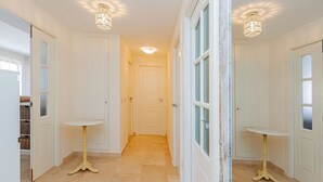 A hallway with white walls, a tiled floor, and two small round tables with gold bases. - Jardin Sweet Apartment (Finestrat)