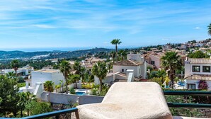 A terrace with a stone bench overlooking a coastal town with Mediterranean architecture, palm trees, and a clear blue sky. - Jardin Sweet Apartment (Finestrat)