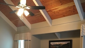 A bedroom with a bed, a ceiling fan, a window with curtains, a painting on the wall, and a wooden headboard. - 3BR/2BA Stand-alone condo. Close to downtown (Gatlinburg)