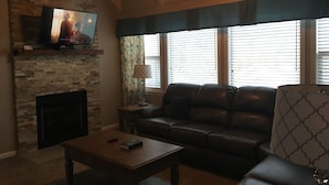 A living room with a stone fireplace, a leather sofa, a coffee table, and a television on a stone wall. - 3BR/2BA Stand-alone condo. Close to downtown (Gatlinburg)