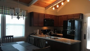 A modern kitchen with dark wood cabinets, a central island with a sink, and a dining area with a table and chairs. - 3BR/2BA Stand-alone condo. Close to downtown (Gatlinburg)