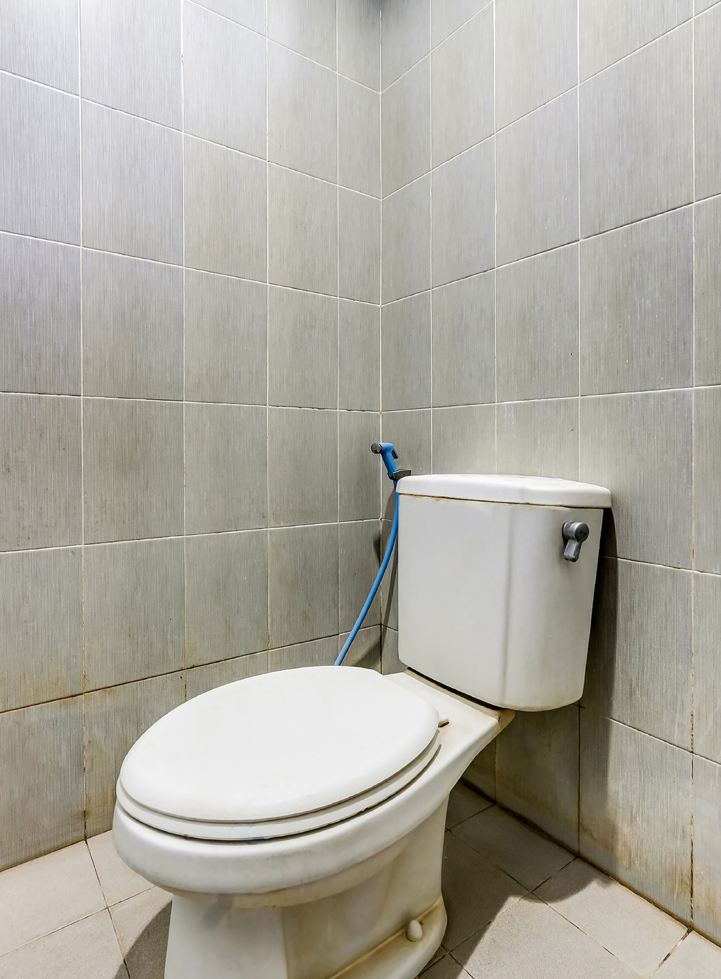 A standard white toilet in a bathroom with grey tiled walls and floor.