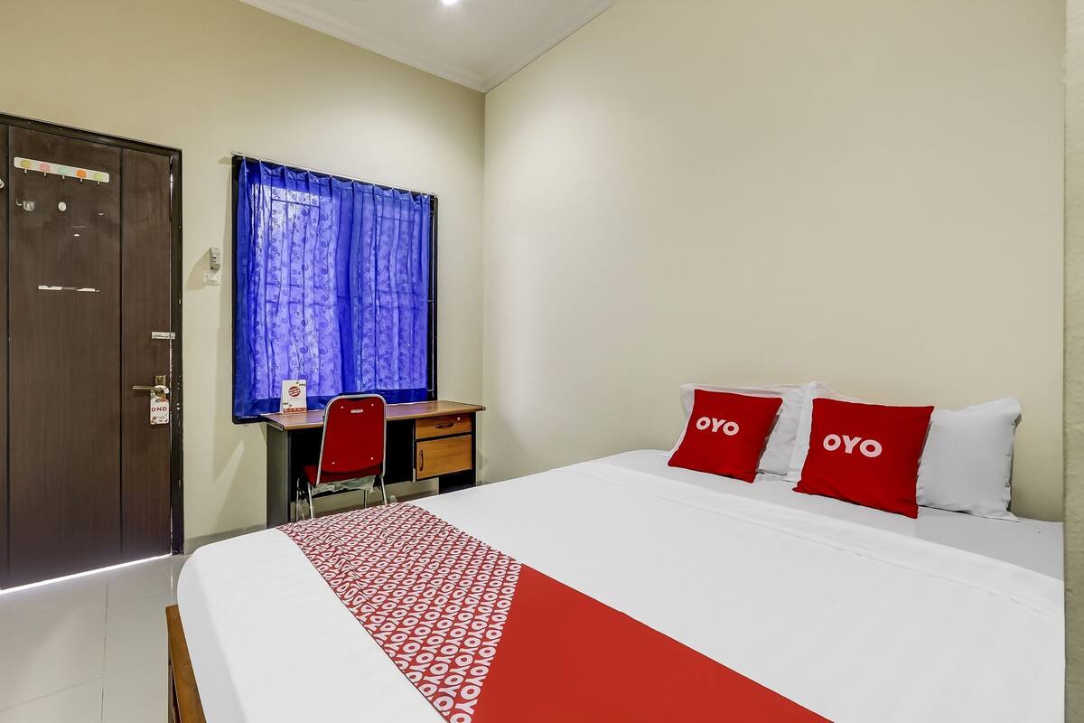 Quarto de hotel com cama, escrivaninha, cadeira e guarda-roupa.