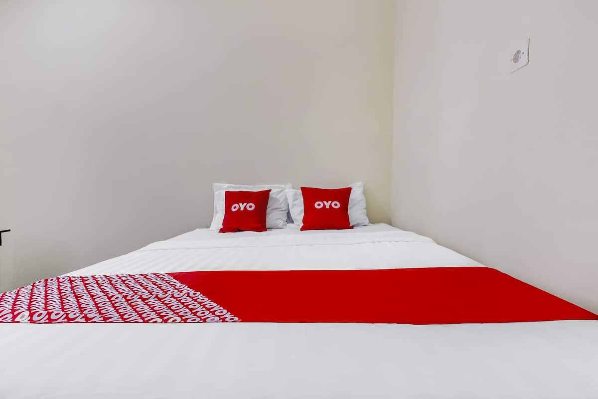 Uma cama com roupa de cama branca e vermelha, dois travesseiros vermelhos com a palavra "OYO" escrita neles e um cobertor com padrão vermelho e branco.