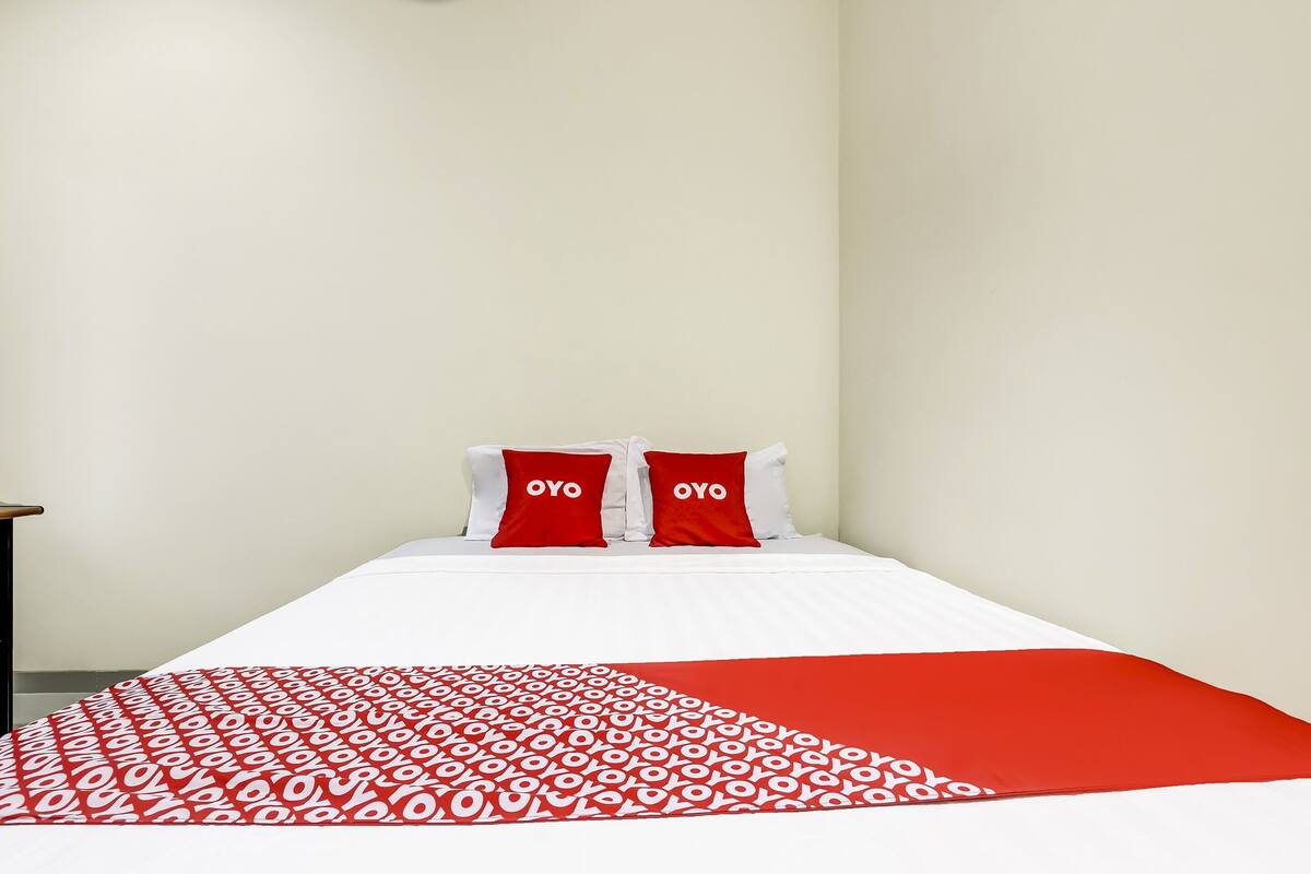 Quarto de hotel com cama, duas almofadas vermelhas com o texto "OYO" e um edredom vermelho e branco estampado.