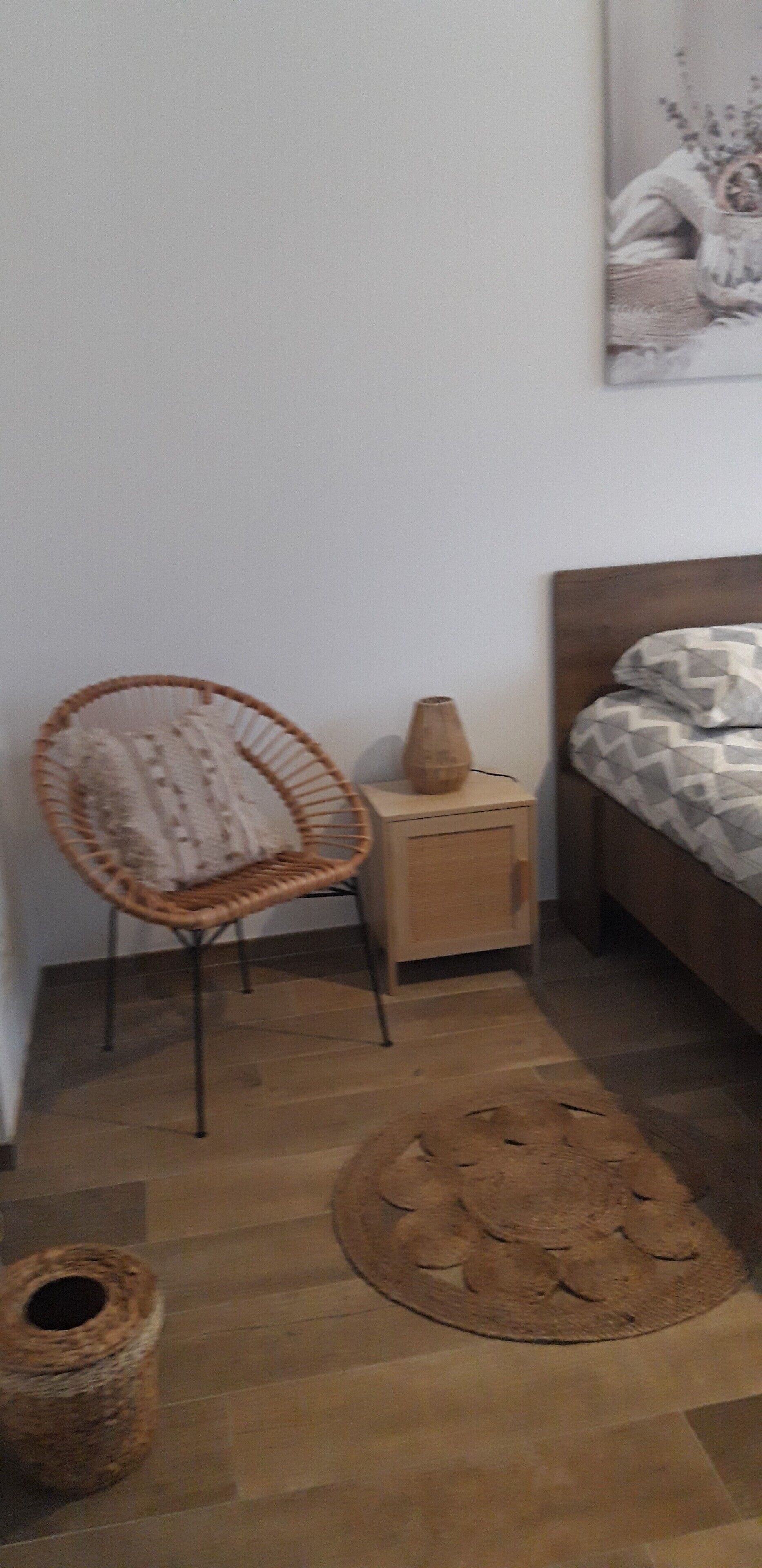 A bedroom with a wooden bed, a wicker chair, a small wooden nightstand, and a woven rug.