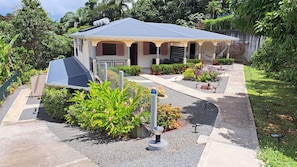 A two-story building with a covered patio, surrounded by landscaped gardens and a gravel pathway.