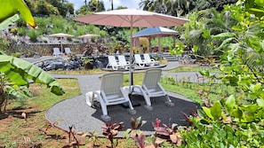A garden area with lounge chairs and umbrellas, surrounded by tropical plants and a gazebo.