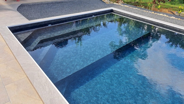 A rectangular swimming pool with clear water, surrounded by a tiled deck and a pebble border. - Paradis Bleu Residence (Petit-Bourg)