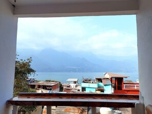 Une vue depuis une fenêtre donnant sur une zone côtière, avec des bâtiments, une étendue d’eau et des montagnes à l’horizon.