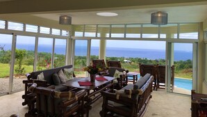 A spacious room with large windows offering a view of the ocean. There is a wooden dining table with chairs and a sofa. - Cabrera oceanview villa (Cabrera)