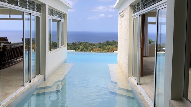 A modern infinity pool with clear blue water, surrounded by glass walls offering a view of the ocean. - Cabrera oceanview villa (Cabrera)