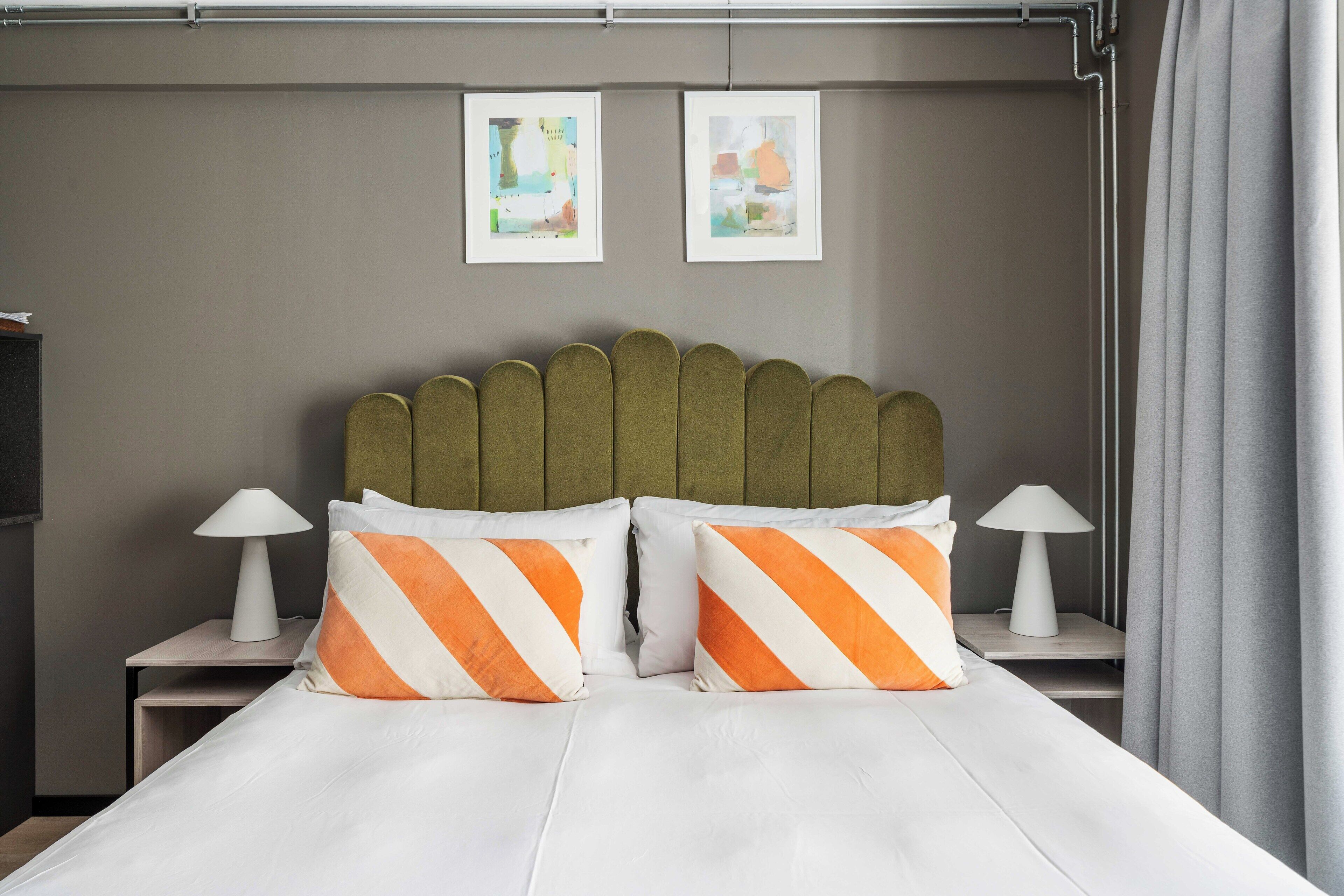 A neatly made bed with striped pillows, a headboard, bedside tables with lamps, and two framed pictures on the wall.