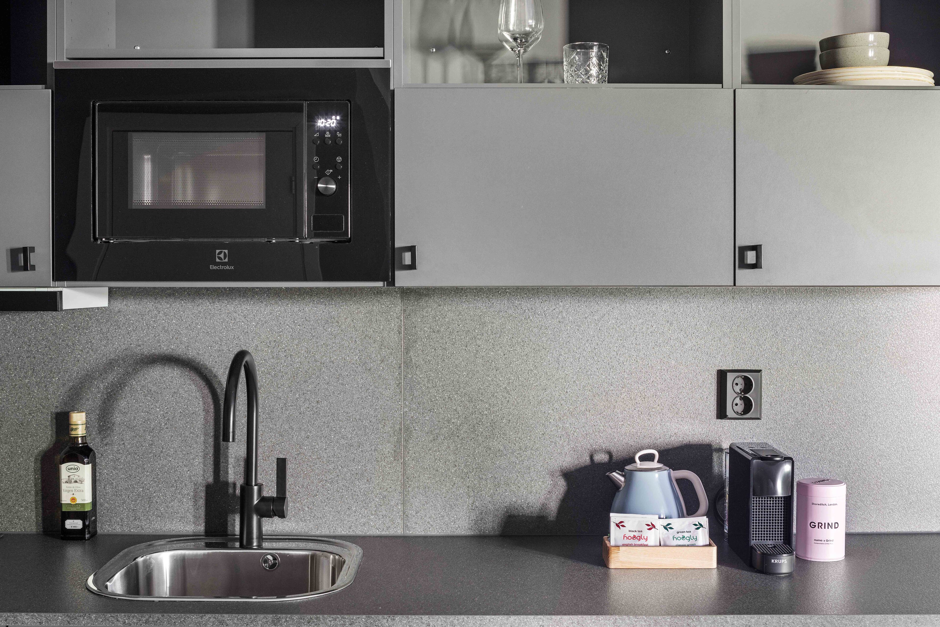 A modern kitchen with a built-in microwave, stainless steel sink, and a kettle.