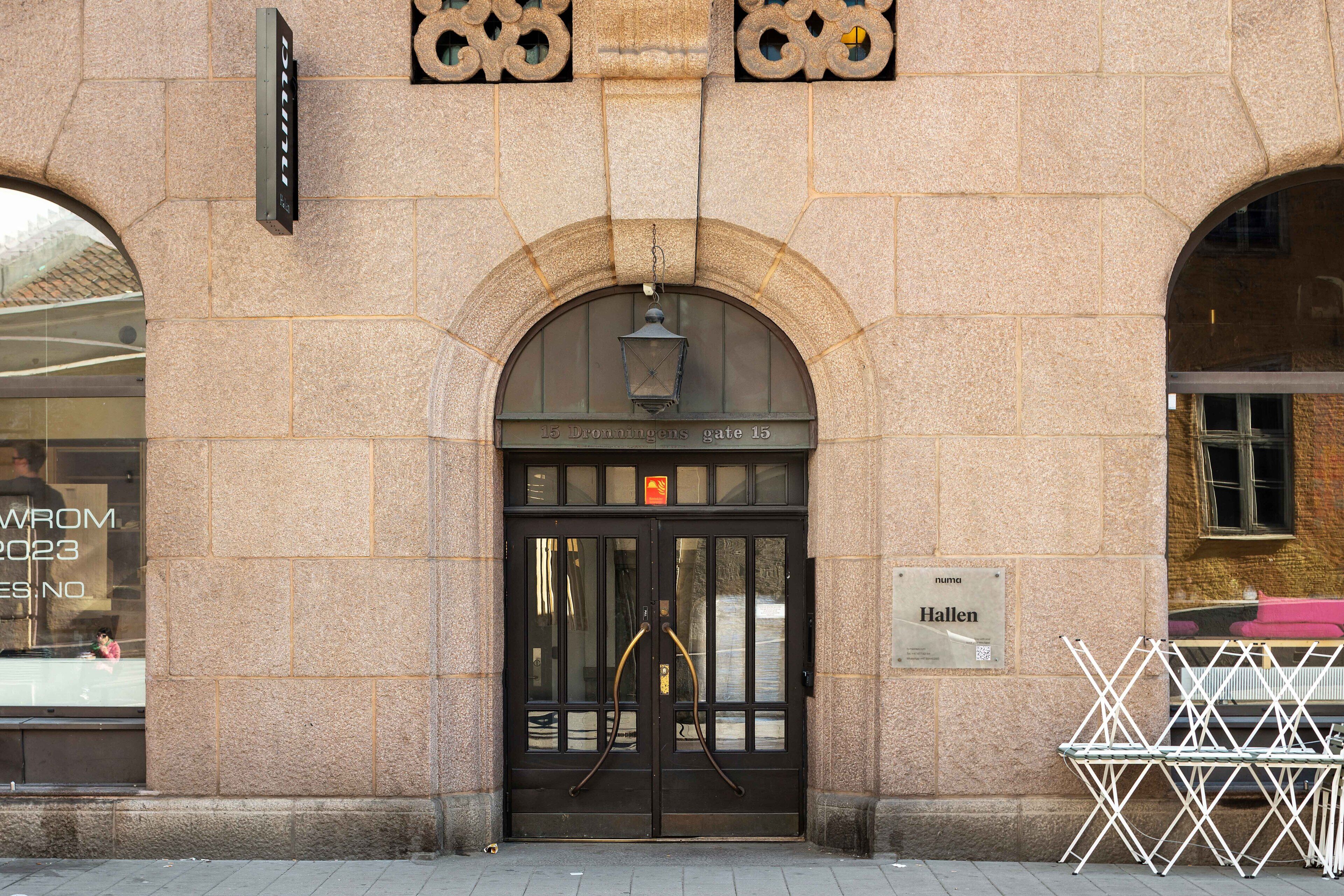 A building entrance with a black door, a sign reading "Hallen", and a small window with a reflection.