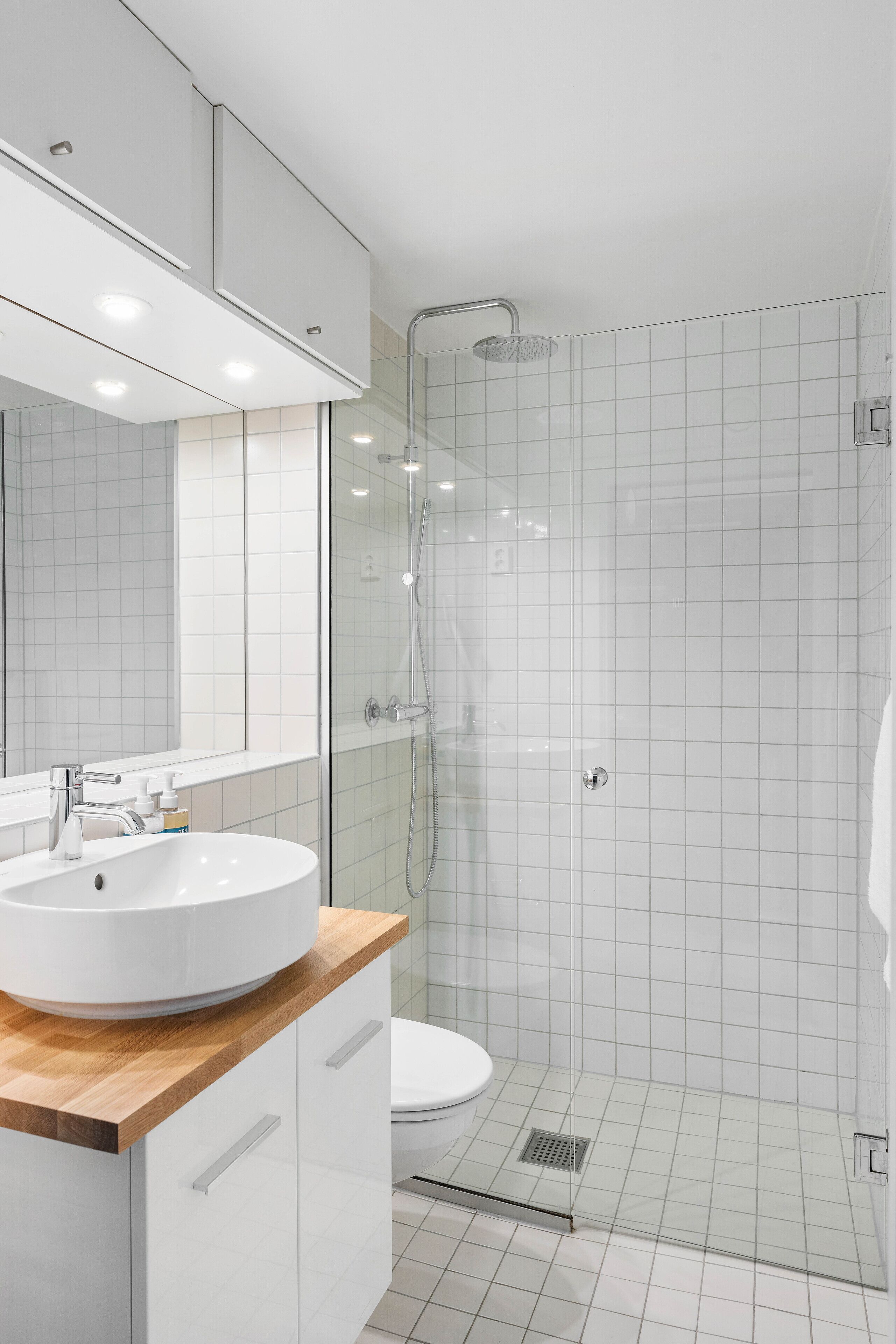 A modern bathroom with a white sink, mirror, and glass-enclosed shower.
