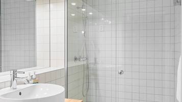A modern bathroom with a white sink, mirror, and glass-enclosed shower.