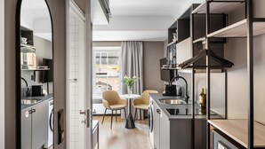 Een compacte keuken met moderne apparatuur, een eethoek met twee stoelen en uitzicht op de straat door een groot raam.