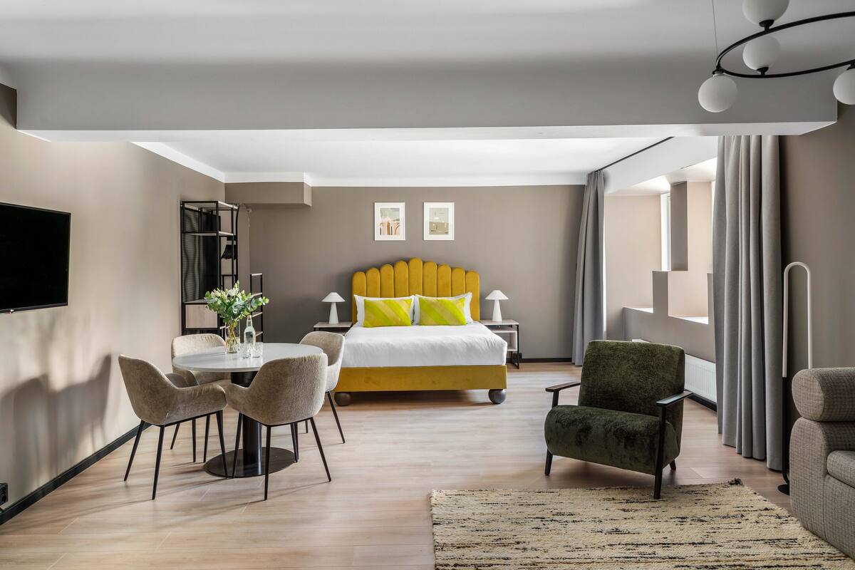Une chambre d’hôtel moderne équipée d’un lit, d’une table à manger avec des chaises, d’un téléviseur et d’une grande fenêtre avec des rideaux.