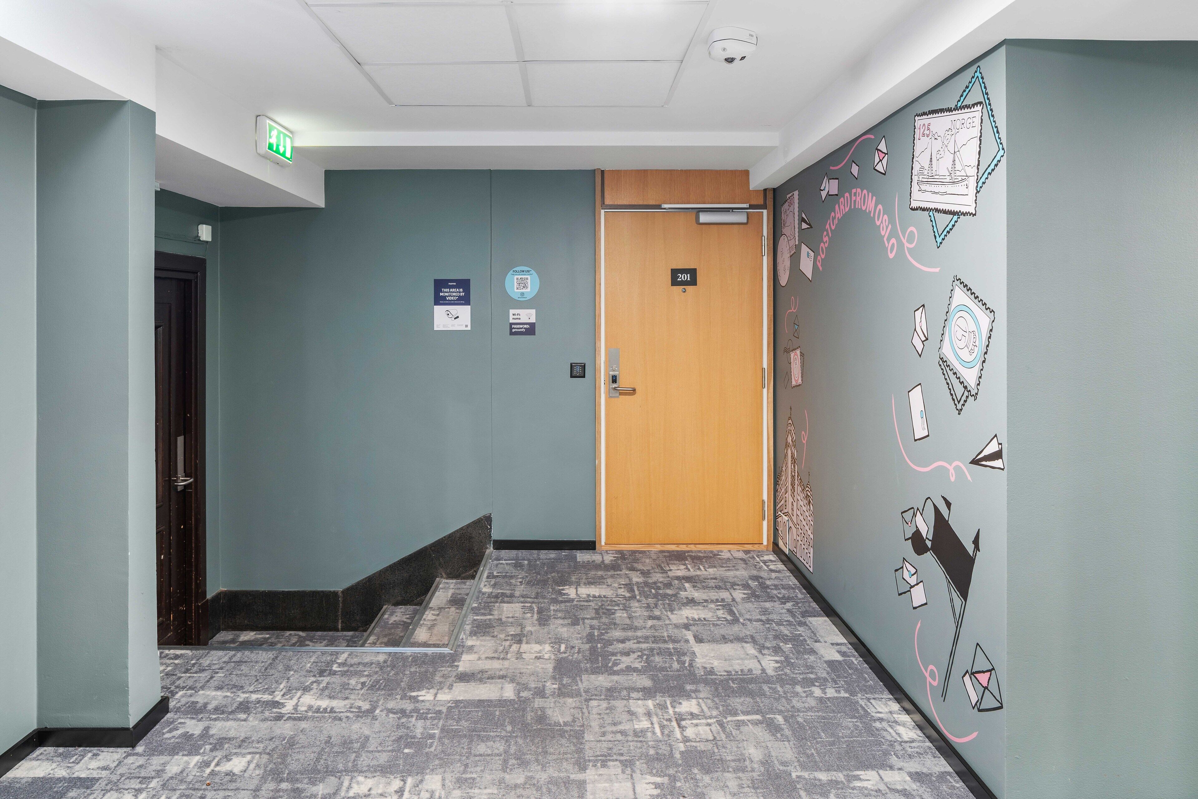 A hallway with a wooden door labeled '201', a blue wall with a QR code, and a patterned carpet.