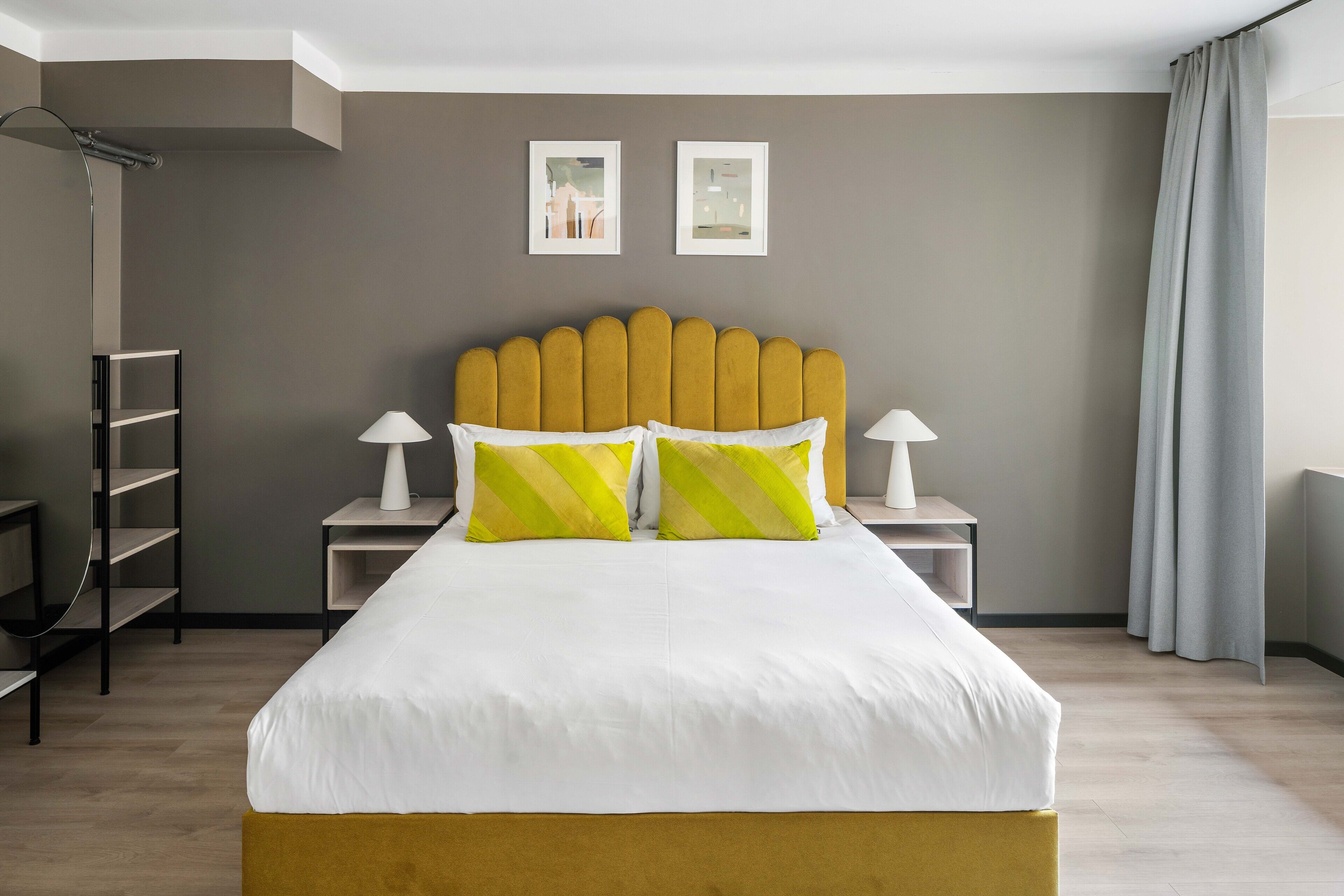 A hotel room with a bed, two bedside tables, a nightstand, a shelf, and a shower area.