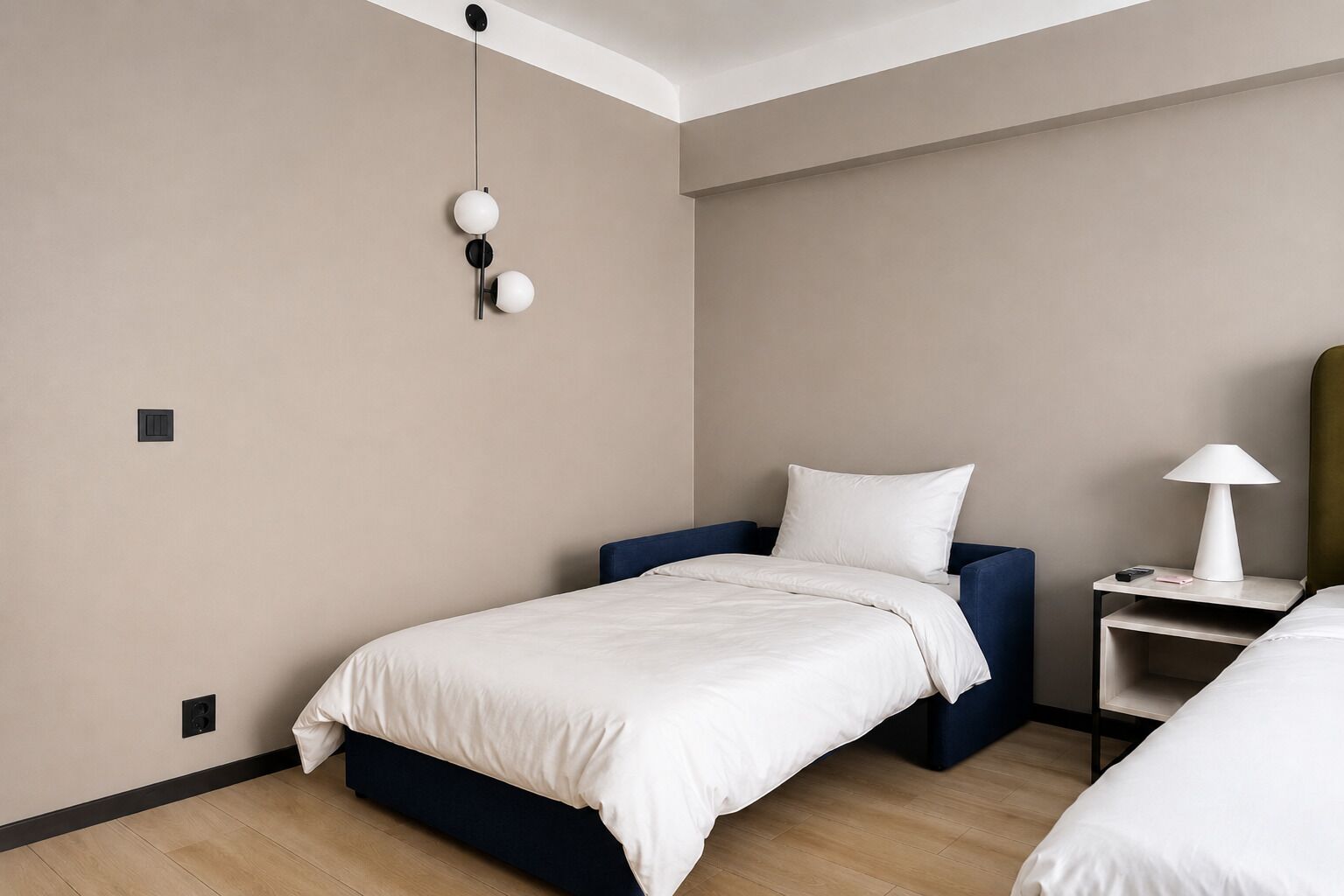 Ein Hotelzimmer mit einem Einzelbett, einem Nachttisch mit Lampe und einer Wandleuchte.
