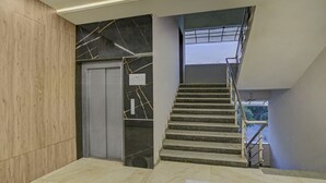 A modern staircase with a metal railing, a door with a lift sign, and a marble wall. - Itsy Hotels Natasha, Vesu, Surat (Surat)