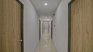 A long, narrow hallway with wooden doors on both sides and a shiny tiled floor. - Itsy Hotels Natasha, Vesu, Surat (Surat)