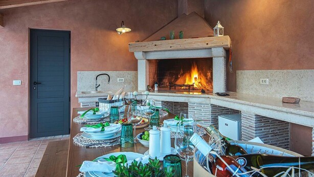 A dining area with a fireplace, wooden ceiling, and a table set for a meal. - Villa Azur – Private pool, wellness, and spacious garden (Muntic)