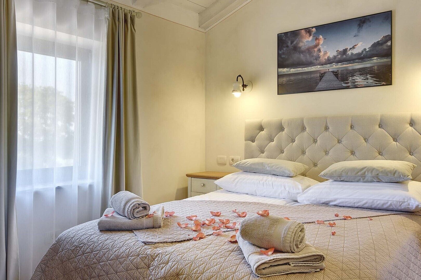 A hotel room with a large bed, a headboard, a nightstand, a wall-mounted lamp, and a painting of a seascape.