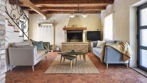 A cozy living room with a fireplace, a TV, and a staircase with decorative iron railings. - Villa Azur – Private pool, wellness, and spacious garden (Muntic)