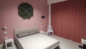 A bedroom with a bed, a white nightstand, a chair, a wall-mounted light fixture, and a curtain. - Exclusive room with bathroom - on Metro A line (Roma)