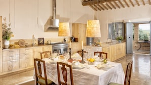 A spacious kitchen with wooden cabinets, a dining table set for a meal, and a large window offering a view of the outdoors. - Recently restored Villa in Tuscany, sleeps 12, sw.pool,  gym, big garden. (San Giovanni d' Asso)