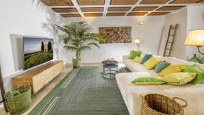 A modern living room with a large flat-screen TV, a sofa with colorful cushions, a green plant, and a wooden bench. - Recently restored Villa in Tuscany, sleeps 12, sw.pool,  gym, big garden. (San Giovanni d' Asso)