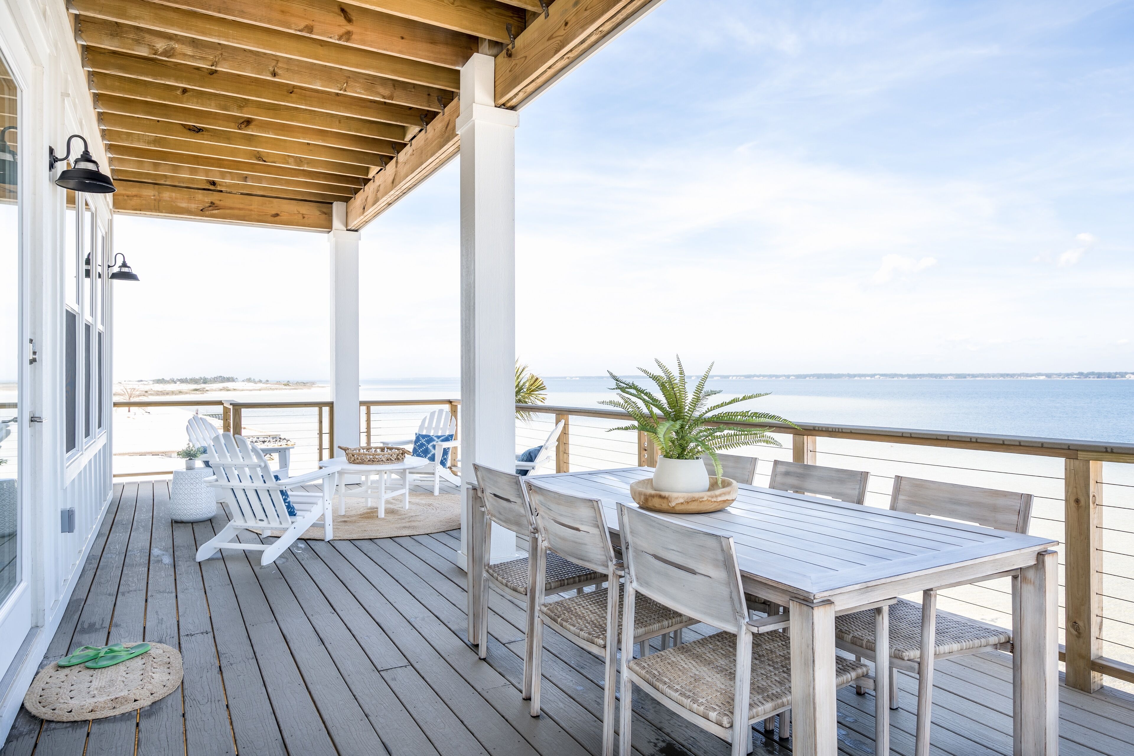 A wooden deck with a table and chairs, overlooking a beach.