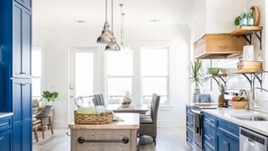 Una cocina moderna con armarios azules, una isla de madera y una zona de comedor con sillas y una mesa.