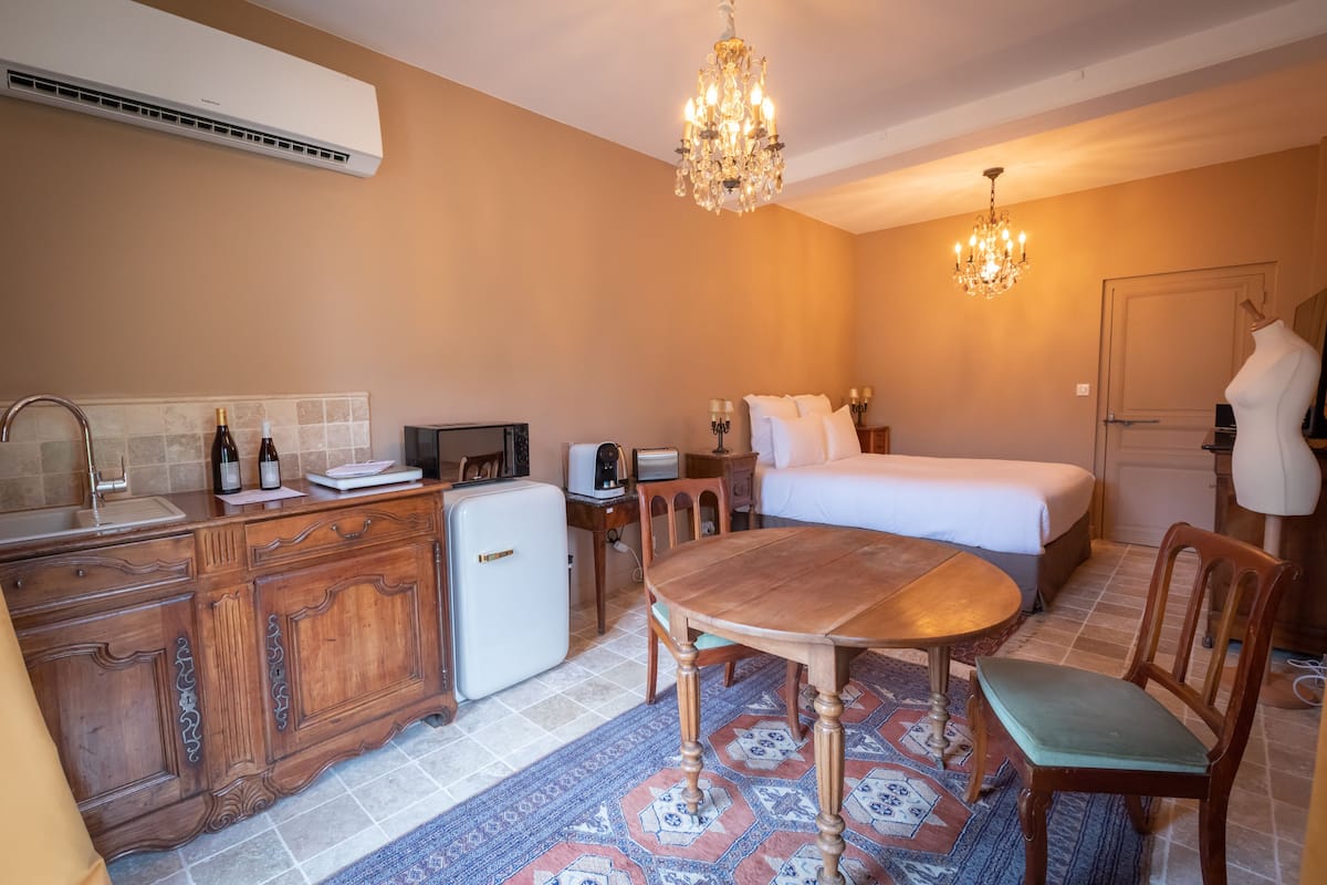 Ein kompaktes Hotelzimmer mit Küchenzeile, einem Bett, einem Esstisch und einem Kronleuchter.