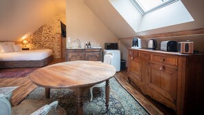 Une chambre à coucher confortable, aménagée en mezzanine avec un plafond en pente, une table à manger en bois, un canapé blanc et un coin cuisine équipé d’appareils électroménagers.