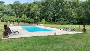 Une piscine rectangulaire, bordée d’une terrasse carrelée et entourée de pelouse et d’arbres.